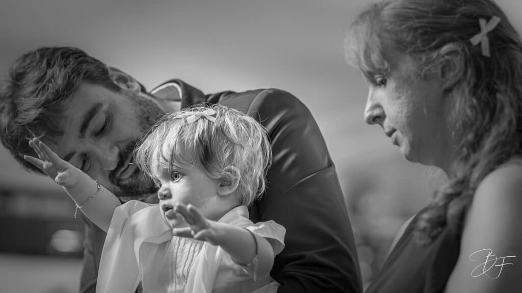 Un père embrasse sa petite fille lors de son baptême, la mère à ses côtés, noir et blanc, par BFO Photographie