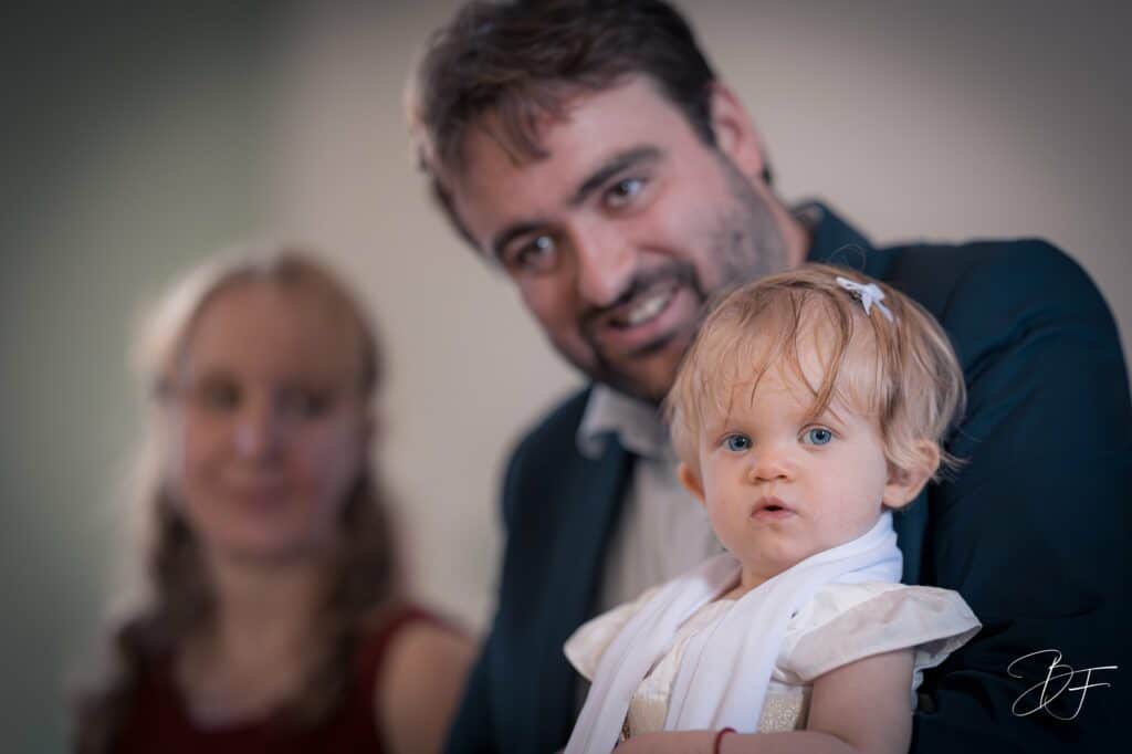 Petite fille aux grands yeux bleus au premier plan, son père souriant derrière elle, par BFO Photographie