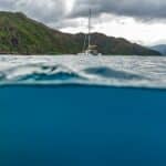Photo demi-sous-marine : plongeur sous la surface, catamaran et montagnes de la Côte Oubliée au-dessus, par BFO Photographie