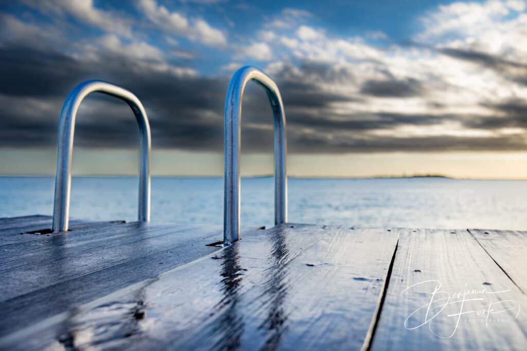 Échelle chromée d'un ponton mouillé face au lagon et à un ciel nuageux, à Nouméa, par BFO Photographie