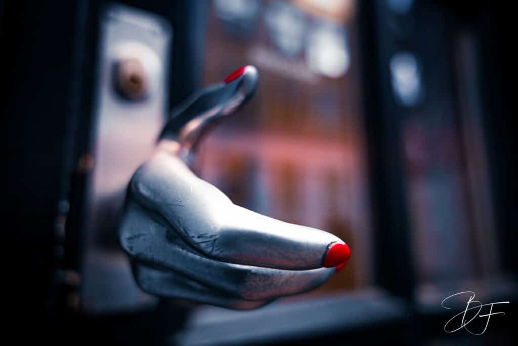 Main sculptée argentée aux ongles rouges vernis, sur fond sombre et flou, image artistique par BFO Photographie