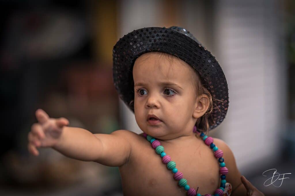 Petite fille coiffée d'un chapeau noir et de colliers de perles, bras tendu, regard concentré, par BFO Photographie