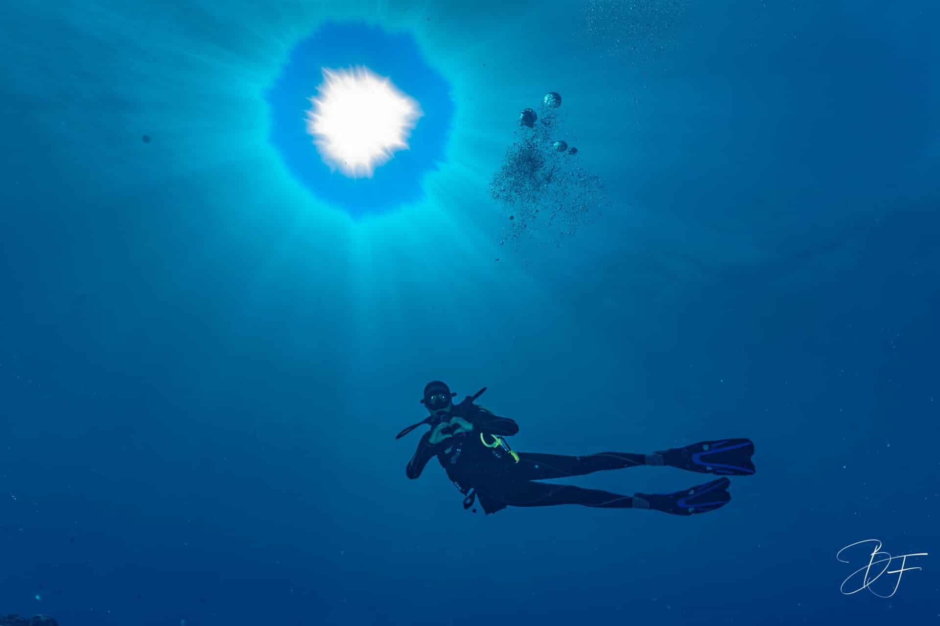 Plongeur en pleine eau sous un soleil étoilé, bulles montantes, près de l'îlot Ténia, par BFO Photographie