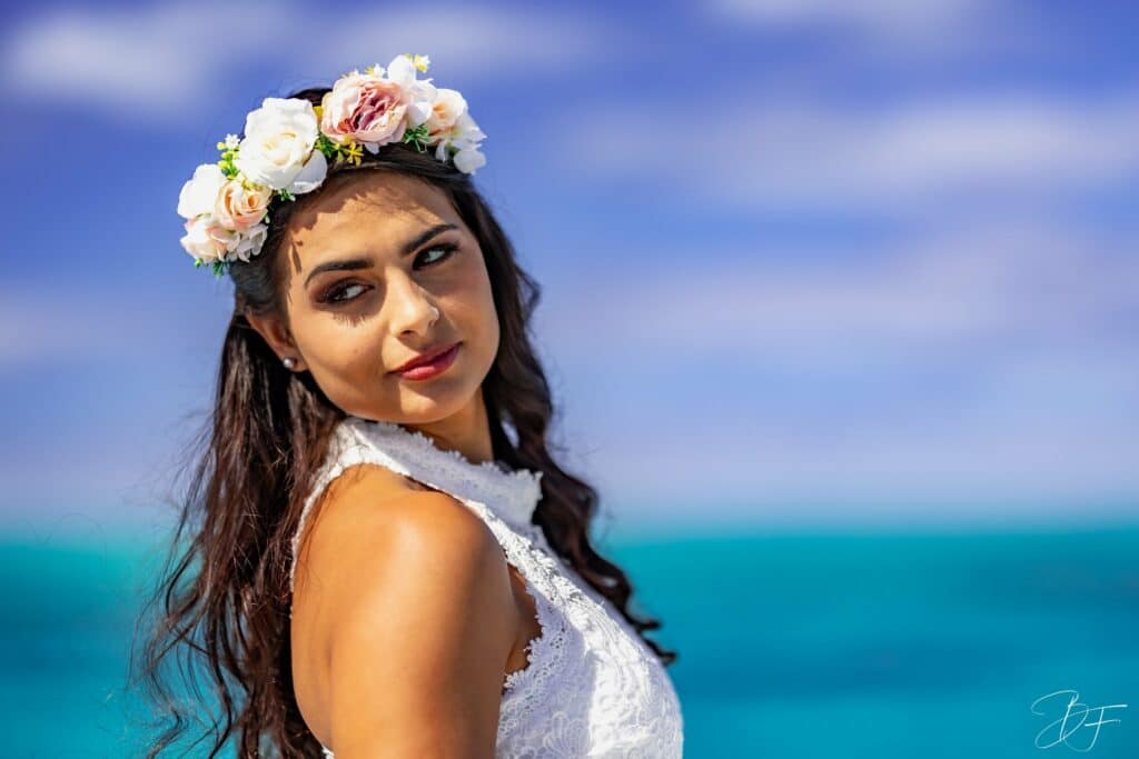 Jeune femme brune portant une couronne de fleurs, regard par-dessus l'épaule devant le lagon, par BFO Photographie