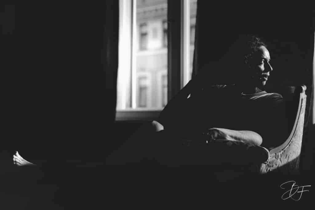 Femme assise près d'une fenêtre dans une pièce sombre, portrait en clair-obscur noir et blanc par BFO Photographie