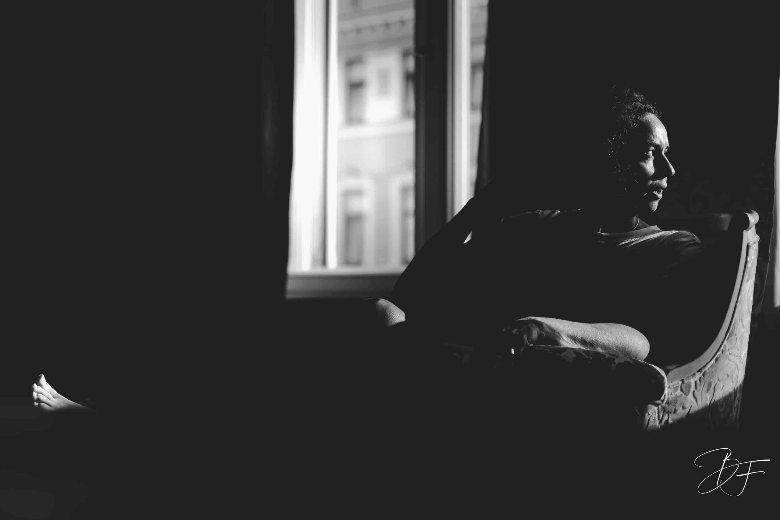 Femme assise près d'une fenêtre dans une pièce sombre, portrait en clair-obscur noir et blanc par BFO Photographie