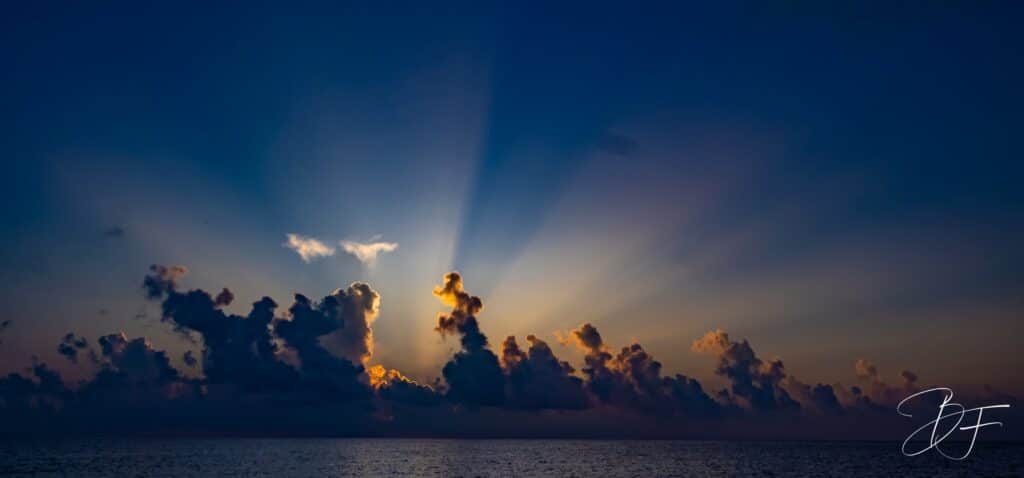 Rayons de soleil jaillissant derrière une ligne de nuages au-dessus de la mer, panorama par BFO Photographie