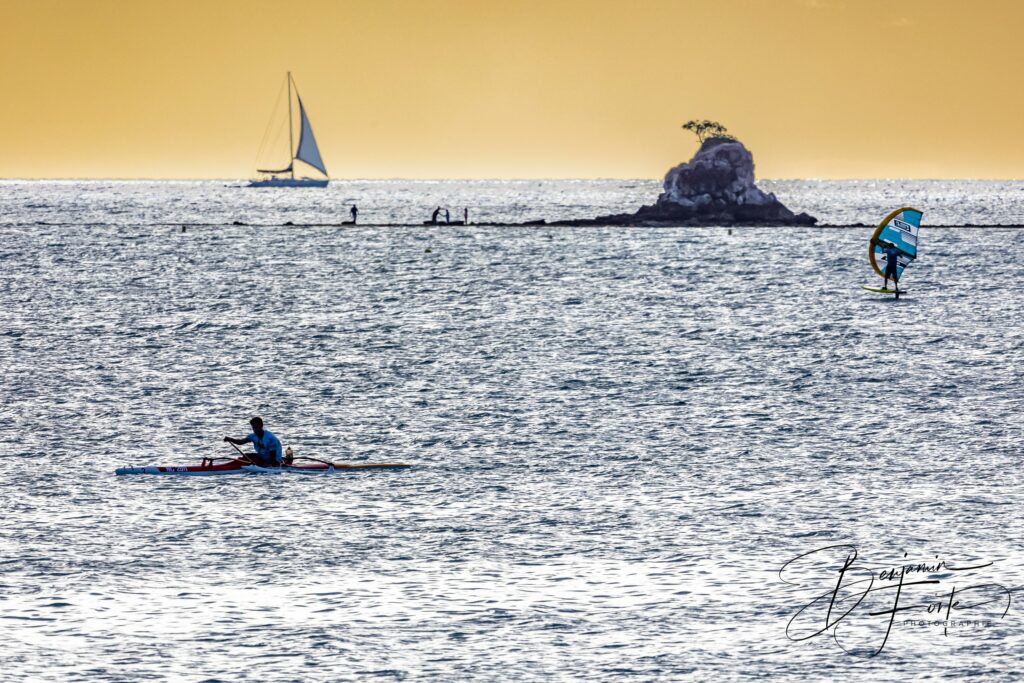 Voilier, wingfoil et kayak autour du Rocher à la Voile sur le lagon de Nouméa, en contre-jour doré, par BFO Photographie