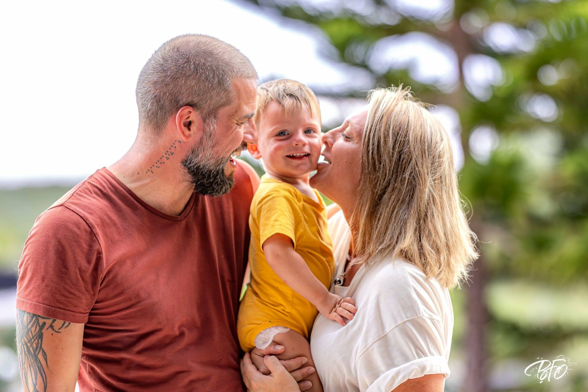 Parents embrassant leur jeune enfant sur les joues, séance photo famille pleine de tendresse par BFO Photographie